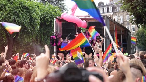 Strasbourg, France - Jun 8, 2019: Sunlight flare over happy crowd of men women people lesbian and gay with gay rainbow flags truck Bisexual Transgender LGBT GLBT dancing techno electro music