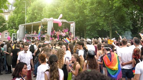 Strasbourg, France - Jun 8, 2019: Sunlight flare over dancing happy crowd of men women people lesbian and gay with gay rainbow flags Bisexual Transgender LGBT GLBT near gay truck with music