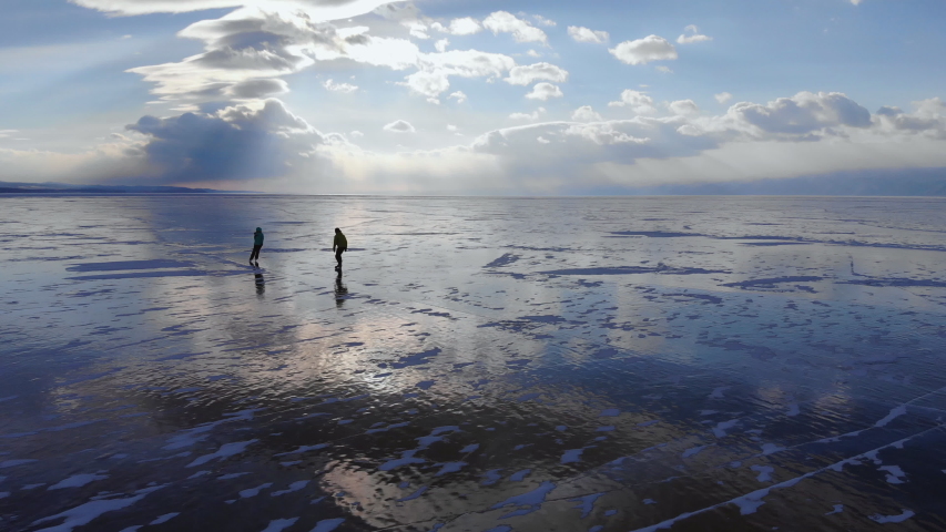 A young couple of travelers skate on the ice of the frozen endless lake.