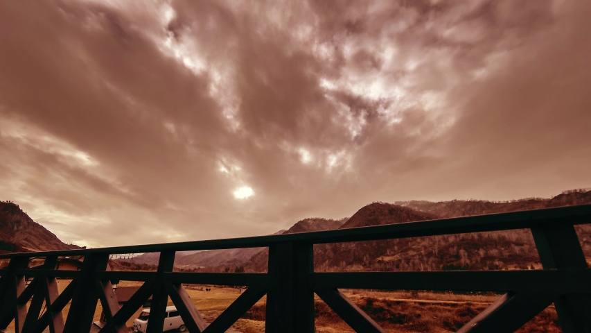 4K UHD time lapse of wooden fence on high terrace at mountain landscape with clouds and sun rays. Autumn or winter weather. Horizontal movement on motorised slider dolly.