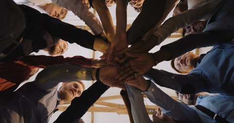 Low angle close-up, happy group of diverse business people put hands together. Teamwork at modern loft office background