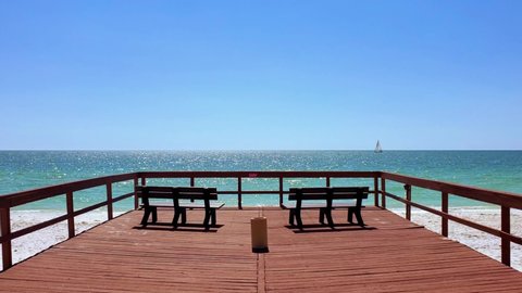 Two wooden benches on a deck facing the beautiful ocean, with waves crashing and a boat moving in the horizon. Clearwater, Florida, USA.
(FYI: footage available from a different angle in my portfolio)