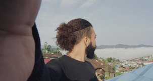 Young African American man taking selfie portrait or video chat to friends back home In Myanmar with Falam mountain village in background.. Slow motion, Shot on Red cinema camera. 