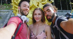 Young happy tourist mixed race friends taking selfie video / photo with smartphone at Asian buddhist temple shrine in Thailand south east Asia. Slow motion travel technology concept. Shot on red.