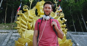 Portrait of young tourist man looking at camera, in front of buddhist shrine in Thailand South East Asia. Shot on red slow motion. 