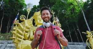 Portrait of young tourist man looking at camera, in front of buddhist shrine in Thailand South East Asia. Shot on red slow motion. 