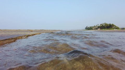 Shallow fast river surface and a beach house among the coconut trees in the background