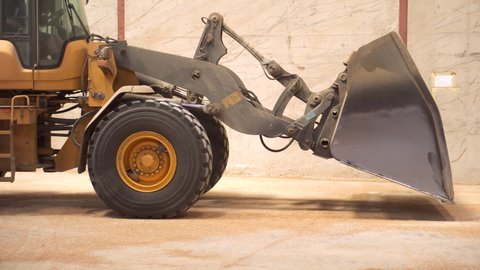 Wheel loader working on construction site. Heavy machinery in warehouse. Wheel bulldozer moving soil in scoop. Close up of excavator bucket .