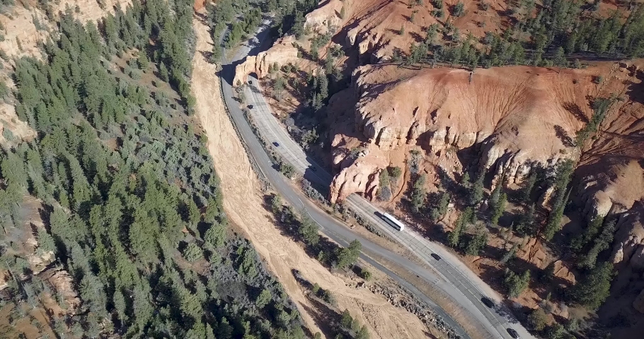 Cars and coaches drive along a scenic road that goes under two naturally formed archways in the Red Canyon of Utah, America.