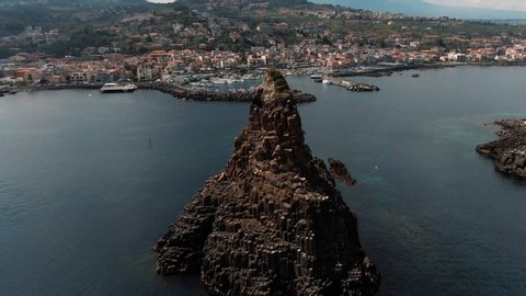 Aerial orbiting view of the faraglioni and the fishing village of Acitrezza