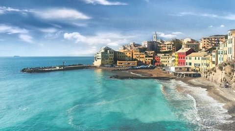 View of Bogliasco, ancient fishing village in Italy, Genoa, Liguria. Turquoise Mediterranean Sea surf, beach and coastal architecture skyline Bogliasco town. Cloudy blue sky sunny day idyllic scenery