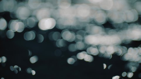 Bokeh sun glare reflected in water surface. Sunrays flickering in water stream. The shimmering small sea waves in sun. Abstract blurry out of focus bokeh background imagery. Slow motion, 4k footage