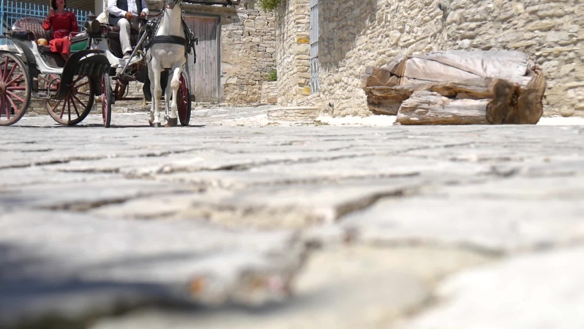 Low angle view of a horse drawn carriage passing two woman on a cobblestone road