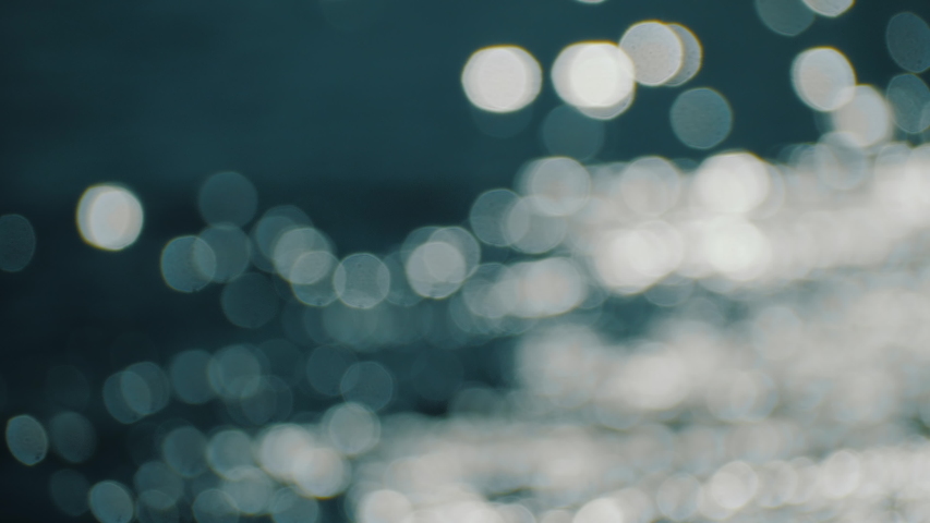Bokeh sun glare reflected in water surface. Sunrays flickering in water stream. The shimmering small sea waves in sun. Abstract blurry out of focus bokeh background imagery. Slow motion, 4k footage.