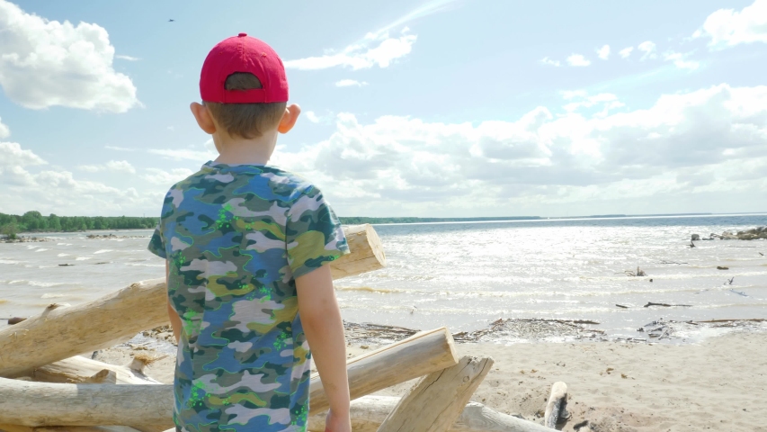 Five-year-old boy walks on the beach, climbs the rocks and snags, catches the wind