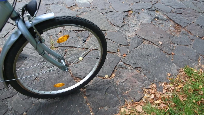 Closeup top view of one front wheel of bike riding isolated on vintage old pavement of city park. Child walking with his bike outdoors. 
