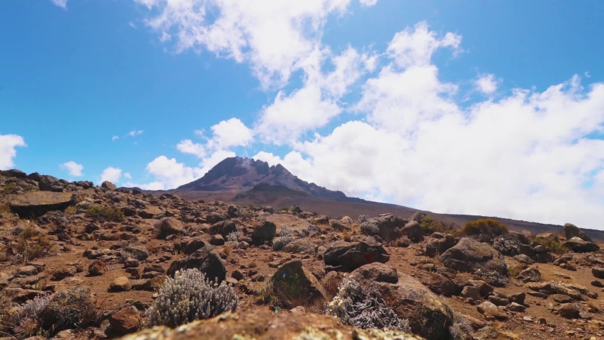 Time lapse shot of rocks, plants and nature, blue sky and the clouds moving above mount Kilimanjaro summit, on a sunny day, in Tanzania, Africa