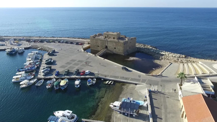 Aerial shot pulling back from Castle Pafos inland revealing boat docks and runners jogging around the port