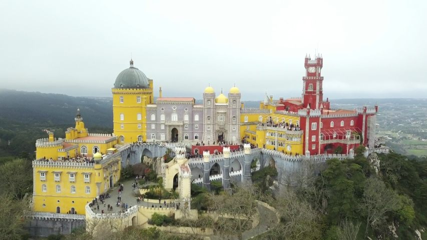 The Pena Palace, a Romanticist castle in the municipality of Sintra, Portugal, Lisbon district, Grande Lisboa, aerial view, shot from drone. Camera moves away, the lock draws in with fog, cloud