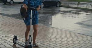 Young woman waking at the rain. Attractive girl returning home with the electric kick scooter. 4K slow motion raw video footage 60 fps