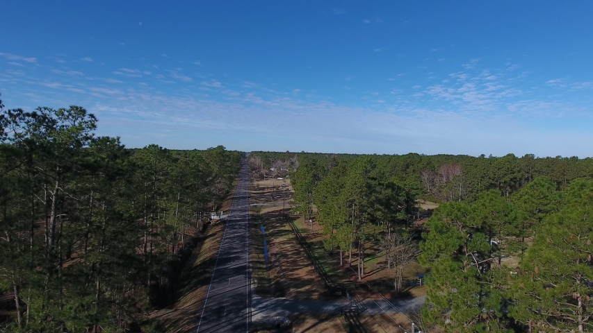 Drone shot rising above a back road in North Carolina towards a beautiful blue sky. The forest runs for miles as far as the eye can see.
