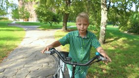 Closeup view of happy white kid walking near his bike after riding outdoors in green city park. Real time full hd video footage.