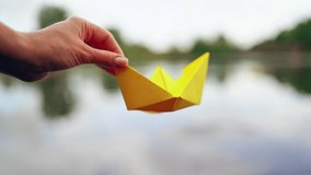 Woman's hand launches paper boat on the water. Paper boat sails along the river.