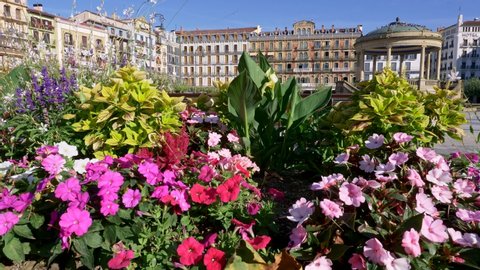 Pamplona, Spain. Bright colored flowers by a bench on a Plaza del Castillo. Lifting shot over flowers to get a wide view of the place. 4K