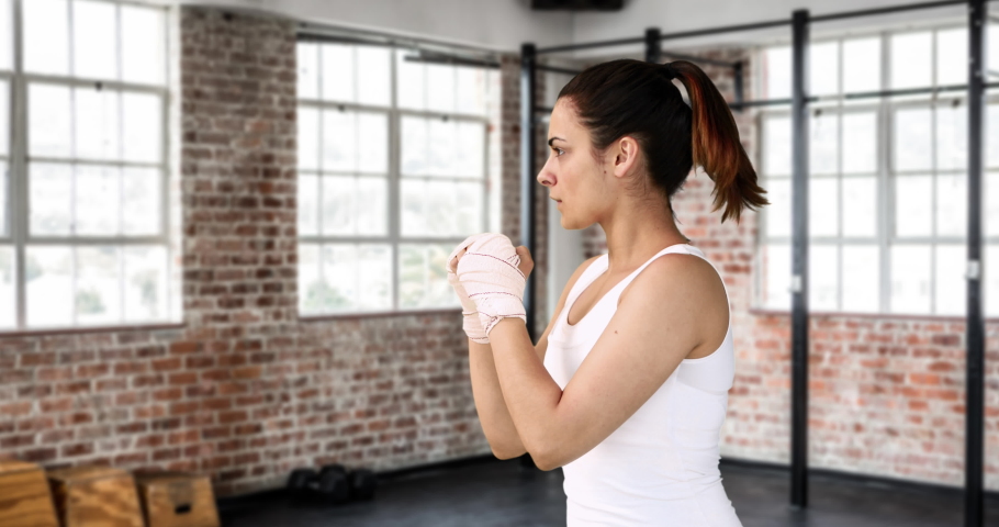 Digital composite of side view of a Caucasian woman wearing a tank top shadowboxing in a gym