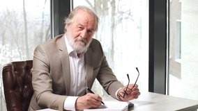 Old professor with grey hair and beard in beautiful suit taking notes in the notebook - Powered by Shutterstock - Get 15% off with code: PIKWIZARD15
