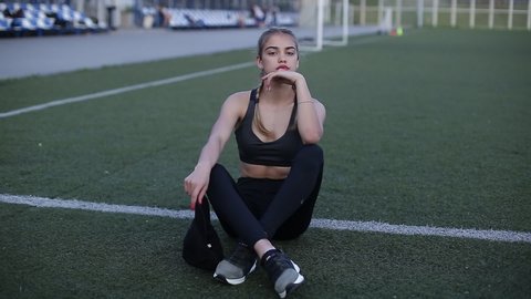 Video portrait of a girl at the stadium. girl with a beautiful athletic figure dies after a workout. The girl in sportswear puts a cap on her head.