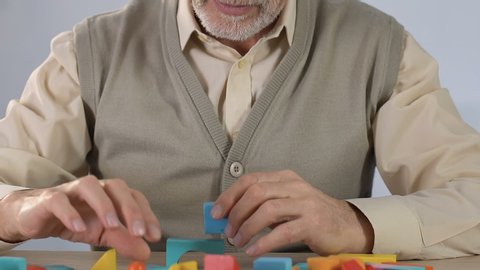 Aged sick man doing well in making house of wooden figures, dementia therapy