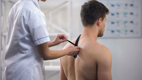 Physician applying Y-shaped tapes on patient upper back, reduce muscle tension
