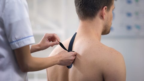Experienced doctor applying Y-shaped tapes on patient upper back, healthcare