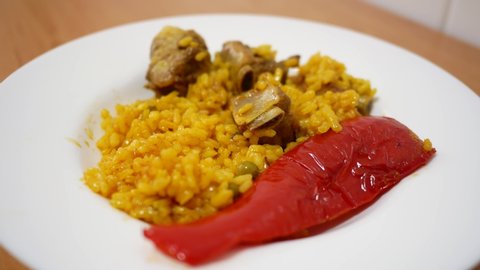 Fork catching rice with meat and red pepper on white plate. Typical spanish paella