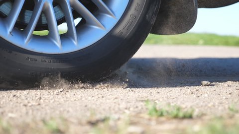Wheel of car are slip on a dirt road during start of movement. Small stones and dirt is fly out from under the tire of a auto. Vehicle quickly beginning motion.Concept of burnout. Slow motion Close up