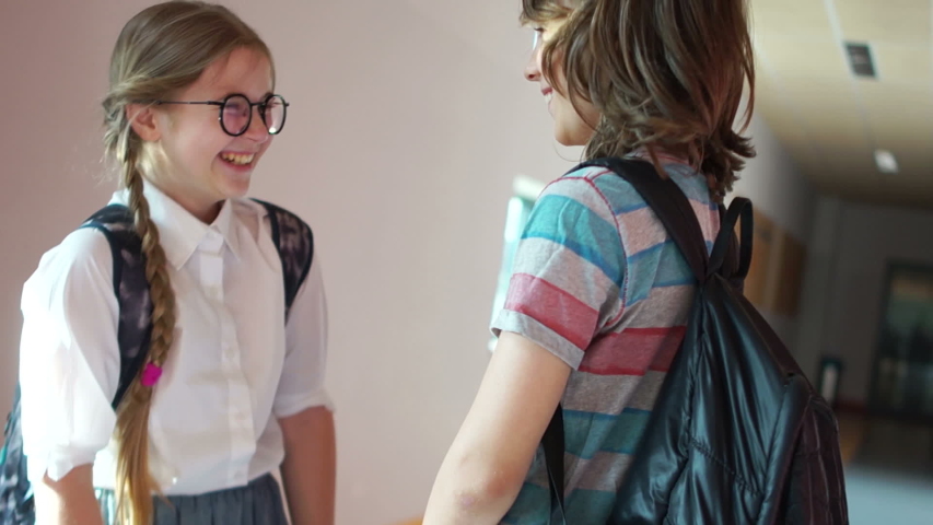 Classmates talk in the school hallway, two schoolchildren with backpacks, back to school, school friendship