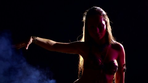beautiful young woman is performing movements of oriental exotic belly dance in darkness
