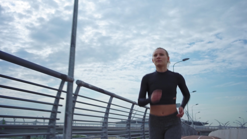 Dolly shot of determined female athlete in sportswear running on bike and walk path on bridge road near railing
