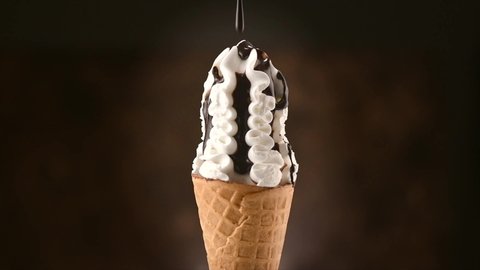 Ice cream cone close-up. Pouring chocolate syrup topping on Icecream in waffle cone, rotating on black background. White Sweet dessert closeup, rotation. Slow motion 4K UHD video