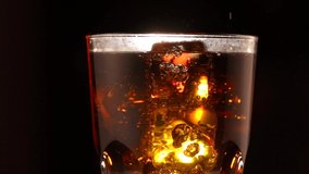 Fizzy Cola with ice cubes background. Coke drink with Ice ,bubbles and water drops on glass. Soda closeup rotating over black background. Food. Rotation Fizzy drink. 4K UHD video footage slow motion