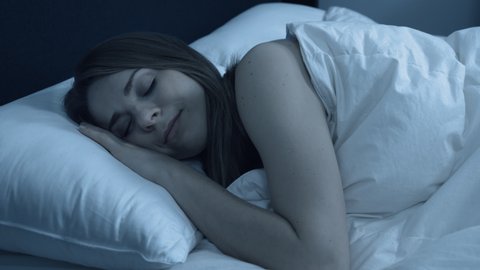 Woman in bed at night smiling, enjoying a restful nights sleep.