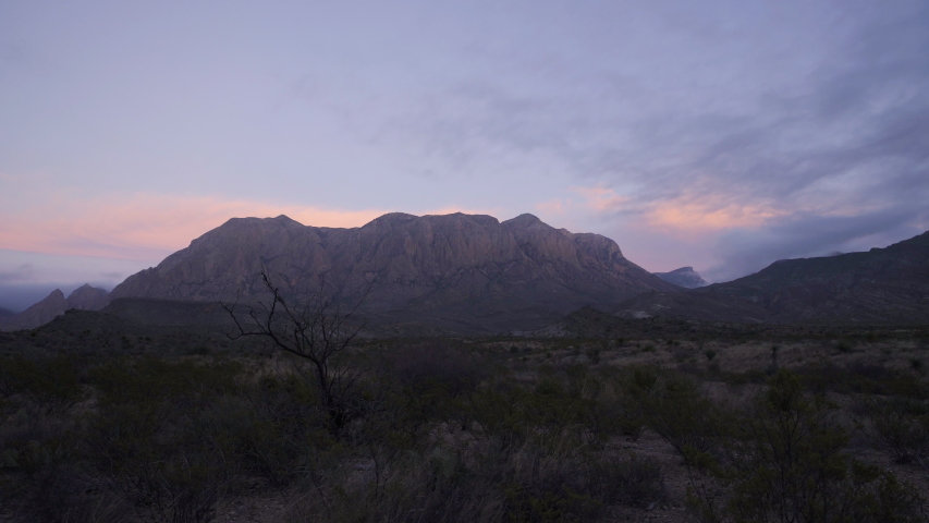 A dry desert landscape at sunset, with high mountain range in the background. Dolly shot left.