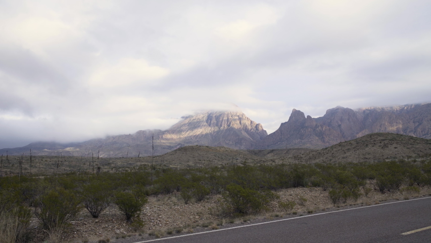 Dolly shot to the left of high misty peaks in the distance, with a vehicle driving through the frame