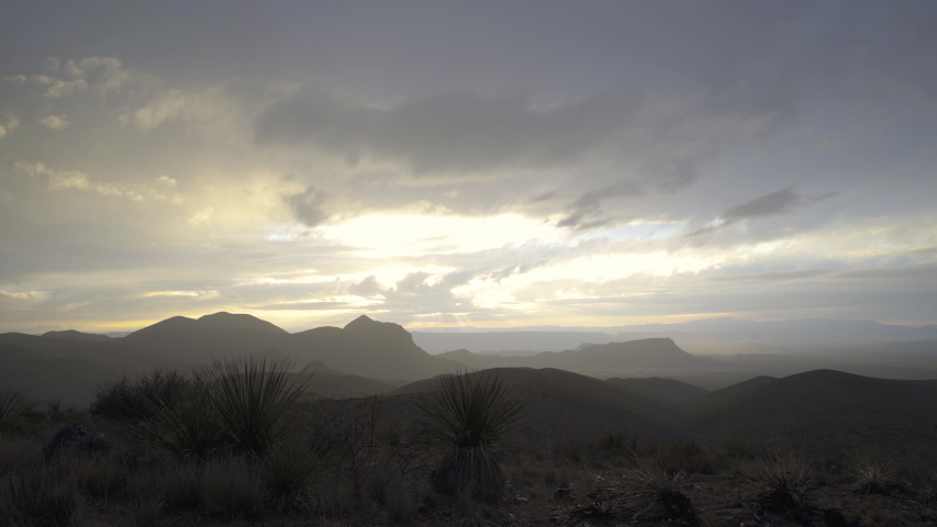 Push in dolly shot in a desert, heavenly glowing cloudscape at sunset over mountains