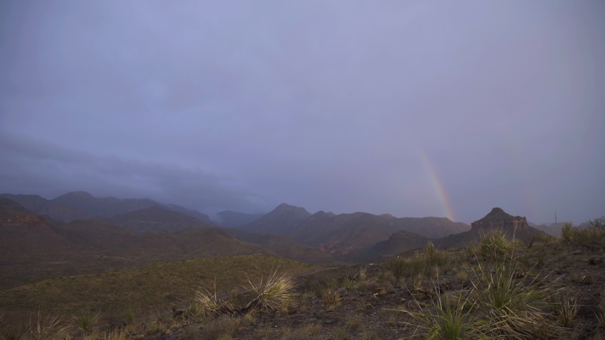 Smooth, stabilized push in dolly shot of a mountain range in the distance with rainbow stretching over the landscape
