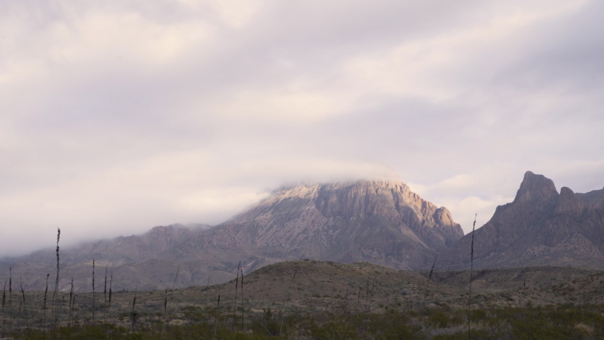 Smooth dolly shot of a mysterious, misty mountain range, clouds covering the tops. Extreme long shot.
