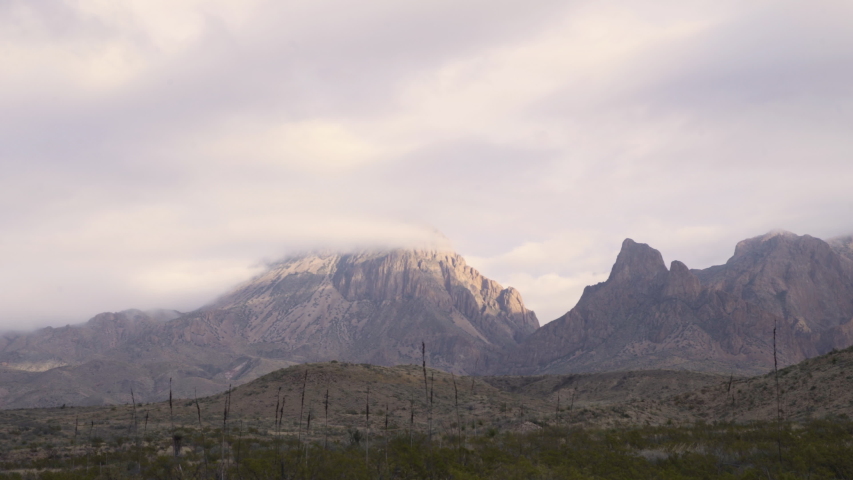 Dolly shot to the right of a high mountain range covered by clouds. Extreme long shot.
