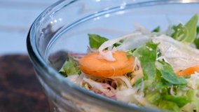 Mix salads and vegetables in glass bowl. Selective focus. Panning to the right.