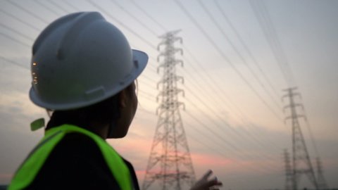 Woman electric Engineering working at High-voltage tower site on sunset